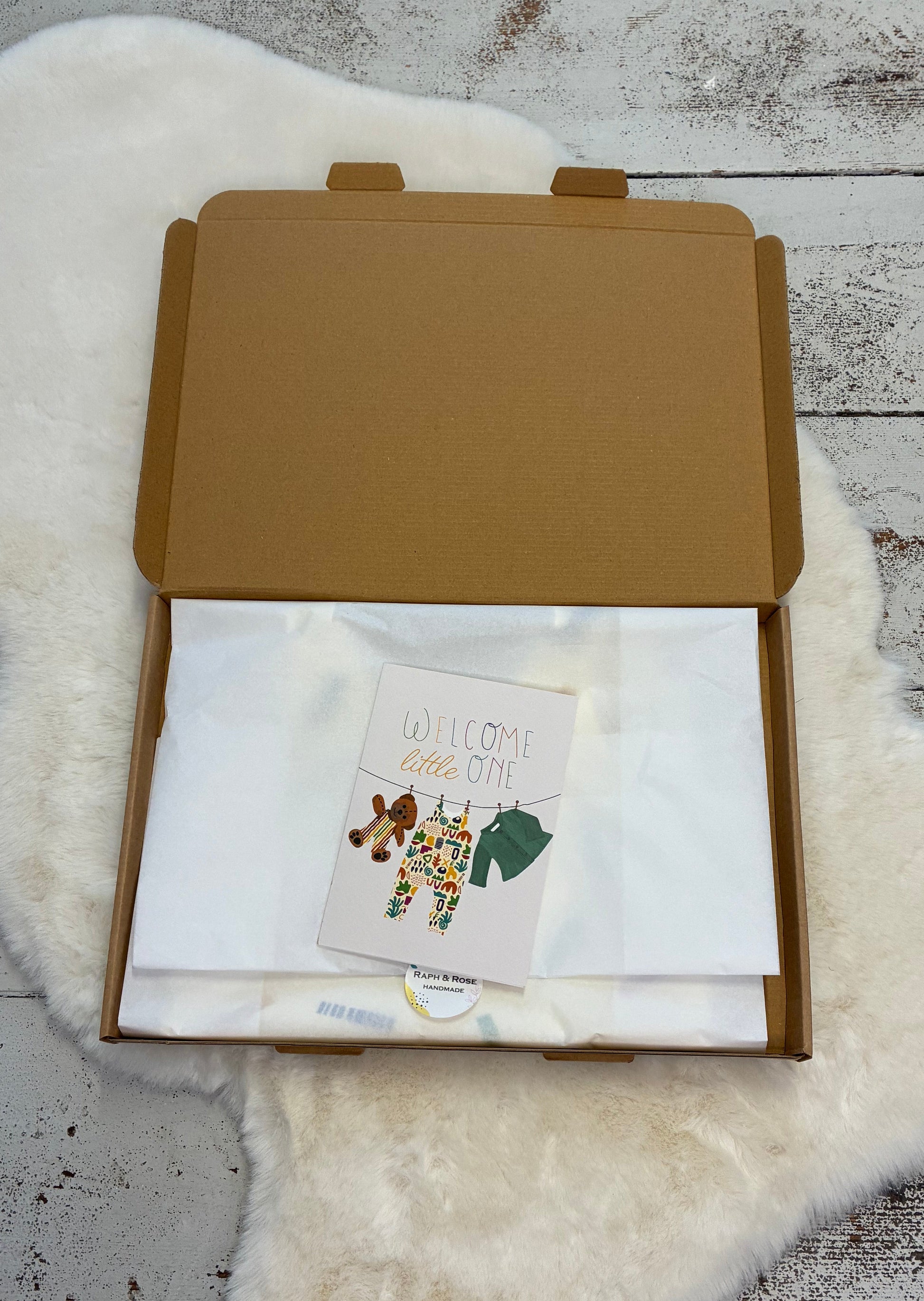 Open brown box on a white fur surface with a card inside
