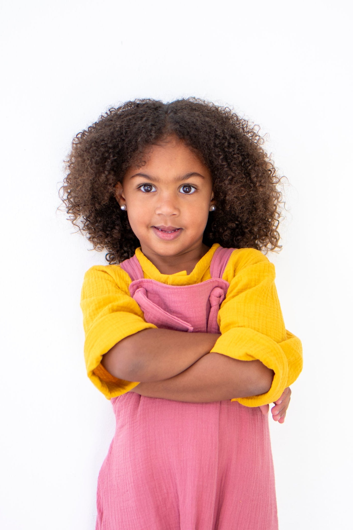 Young girl wearing a yellow shirt and pink dungarees on a white background