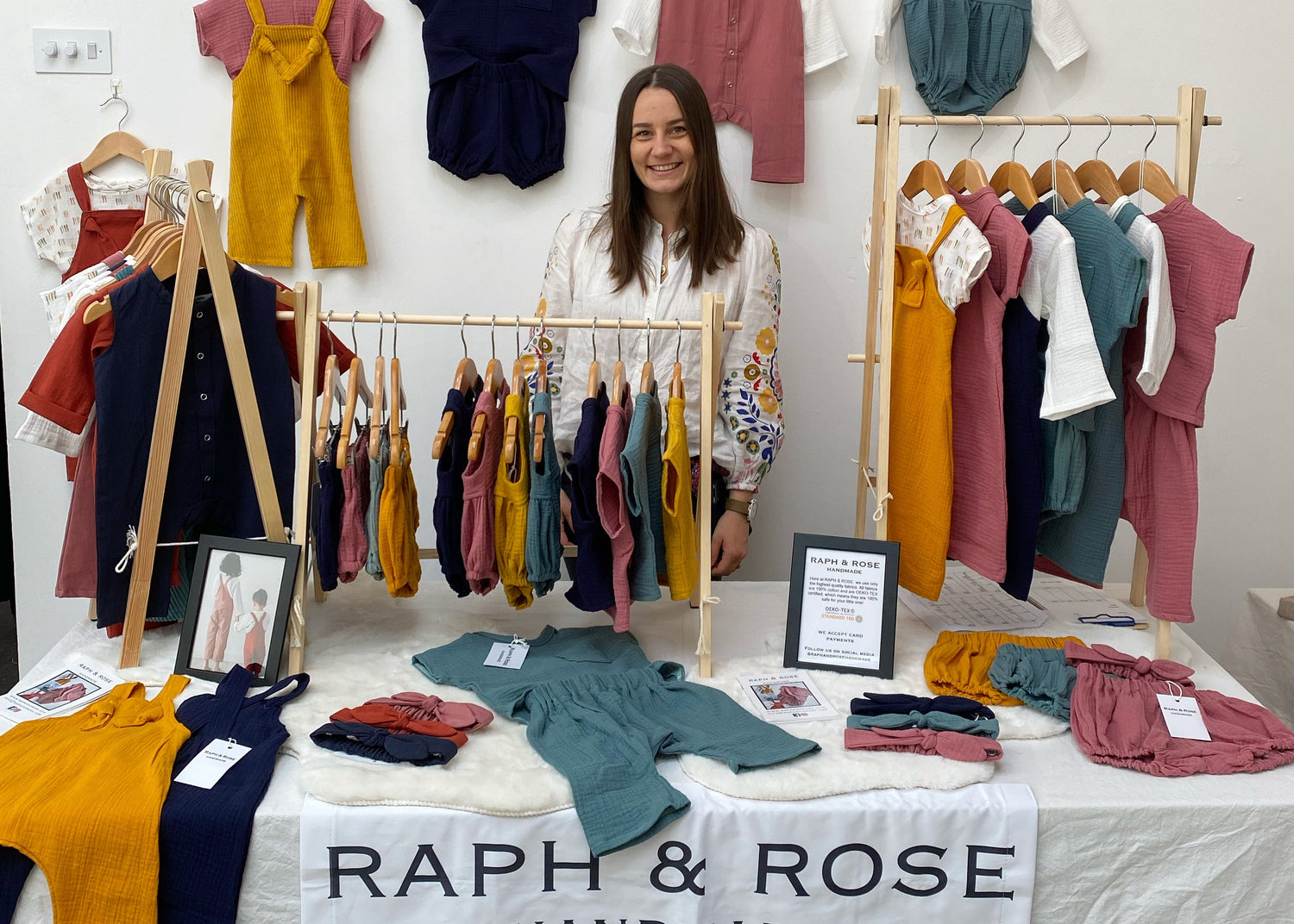 Woman standing behind a display of children's clothing with 'Raph & Rose' branding.